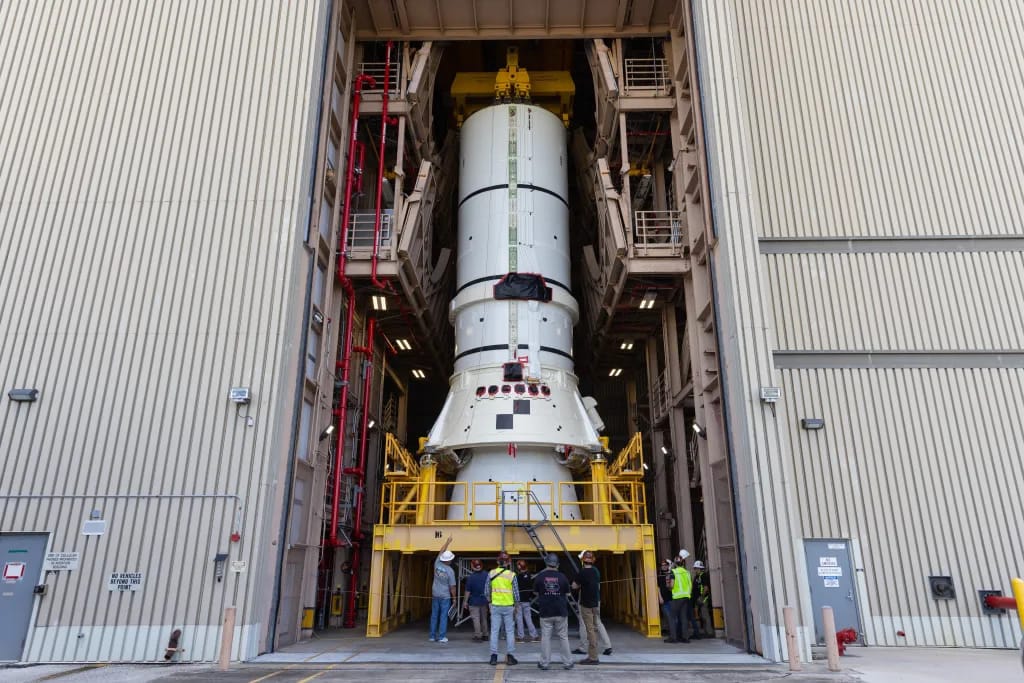 La imagen muestra los segmentos del propulsor apilados dentro del Edificio de Ensamblaje de Vehículos en el Centro Espacial Kennedy de la NASA. Los ingenieros se preparan para transferir uno de los conjuntos de popa de los propulsores del cohete SLS de la misión Artemis II con una grúa aérea.