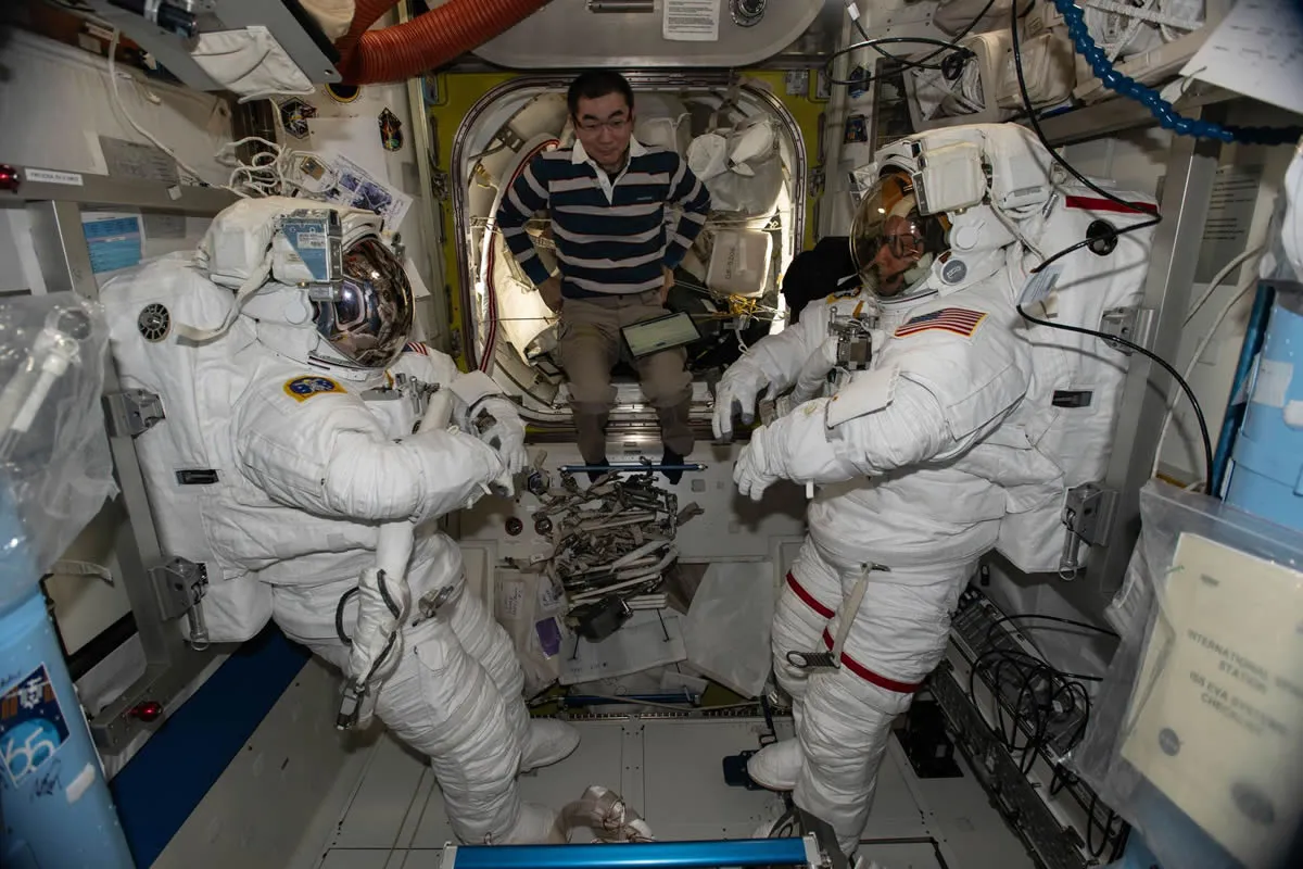 En el centro, el astronauta Kimiya Yui de JAXA (Agencia Japonesa de Exploración Aeroespacial) asiste a los astronautas de la NASA Zena Cardman (izquierda) y Mike Fincke (derecha) durante las inspecciones de los trajes espaciales dentro de la esclusa Quest de la Estación Espacial Internacional.