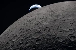 La superficie lunar llena el encuadre con detalles nítidos durante el sobrevuelo lunar de Artemis II, mientras se observa una Tierra distante poniéndose en el fondo. La imagen fue tomada a las 22:41 GMT, apenas tres minutos antes de que la nave Orión y su tripulación pasaran detrás de la Luna, perdiendo contacto con la Tierra durante unos 40 minutos antes de emerger por el otro lado. En la imagen, la parte oscura de la Tierra está en plena noche, mientras que en el lado diurno se distinguen nubes arremolinadas sobre Australia y Oceanía. En primer plano, el cráter Ohm presenta bordes en forma de terraza y un fondo relativamente plano marcado por picos centrales, formados cuando la superficie lunar se elevó tras el impacto que originó el cráter. En el momento de la fotografía, la nave se encontraba aproximadamente a 58,400 km de la Luna y 380,000 km de la Tierra, ofreciendo una vista cercana y única tanto del terreno lunar como del planeta.