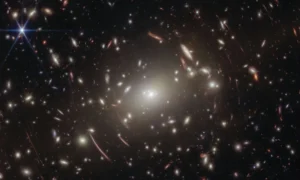 Los astrónomos estaban usando el telescopio James Webb para estudiar un cúmulo de galaxias llamado Abell S1063 y buscar ciertas estrellas. Sin embargo, mientras analizaban las imágenes y datos recogidos, también encontraron información muy detallada sobre un objeto distante llamado GLIMPSE-17775. Este objeto aparece como un pequeño punto rojo en el cielo y está mucho más lejos que el cúmulo de galaxias que estaban observando.