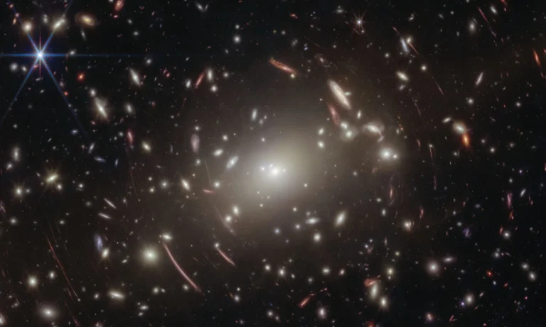 Los astrónomos estaban usando el telescopio James Webb para estudiar un cúmulo de galaxias llamado Abell S1063 y buscar ciertas estrellas. Sin embargo, mientras analizaban las imágenes y datos recogidos, también encontraron información muy detallada sobre un objeto distante llamado GLIMPSE-17775. Este objeto aparece como un pequeño punto rojo en el cielo y está mucho más lejos que el cúmulo de galaxias que estaban observando.